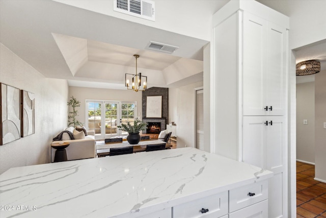 kitchen with a tray ceiling, open floor plan, visible vents, and a lit fireplace