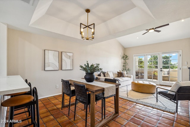 dining space with ceiling fan with notable chandelier, a tray ceiling, dark tile patterned floors, and baseboards