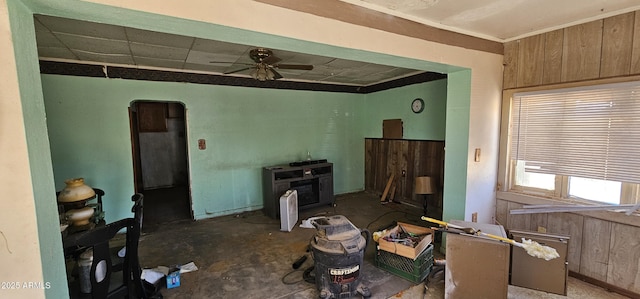 living room featuring ceiling fan, wooden walls, and unfinished concrete flooring