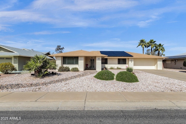 view of front of home with brick siding, roof mounted solar panels, a garage, and driveway