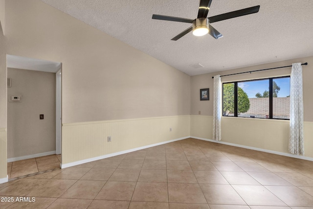 spare room featuring tile patterned flooring, lofted ceiling, wainscoting, a textured ceiling, and a ceiling fan