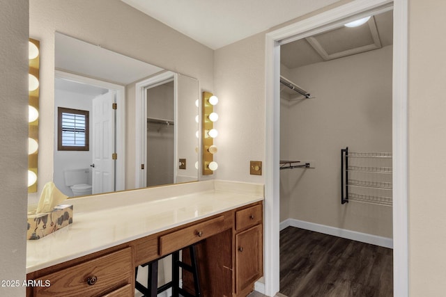 bathroom featuring vanity, a walk in closet, toilet, and wood finished floors