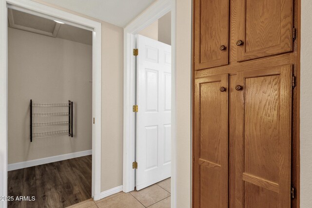 corridor featuring light tile patterned floors, attic access, and baseboards