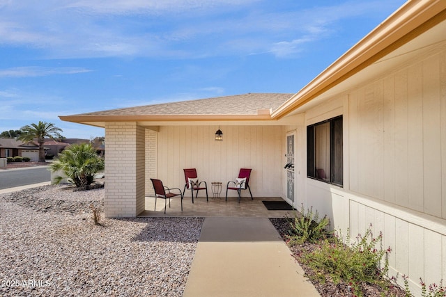 entrance to property featuring brick siding, a patio, and roof with shingles