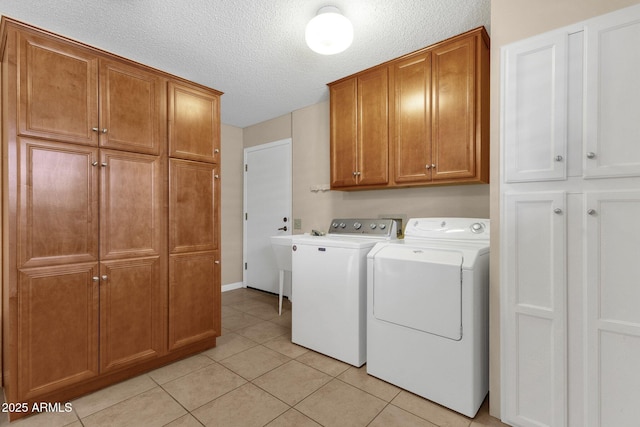 clothes washing area with light tile patterned floors, washing machine and dryer, cabinet space, and a textured ceiling