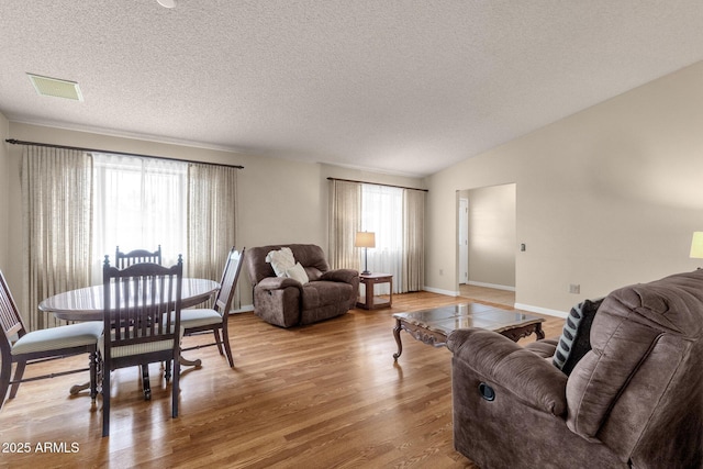 living room featuring light wood-type flooring, visible vents, a textured ceiling, baseboards, and vaulted ceiling