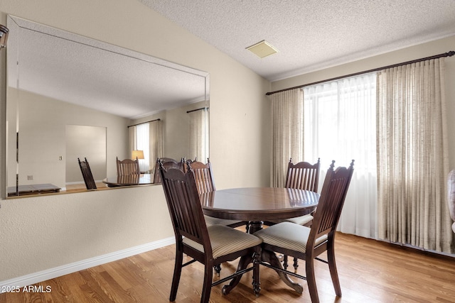 dining room featuring a wealth of natural light, baseboards, light wood-style floors, and vaulted ceiling