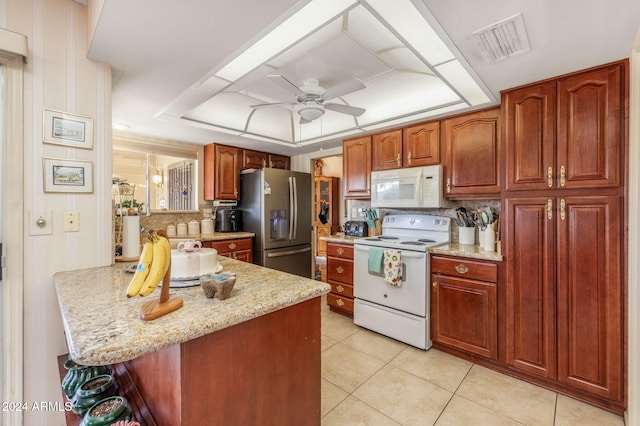 kitchen with ceiling fan, light stone countertops, white appliances, a tray ceiling, and light tile patterned floors