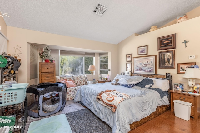 bedroom with lofted ceiling, light hardwood / wood-style flooring, and a textured ceiling