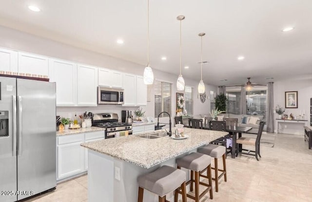 kitchen featuring white cabinetry, a center island with sink, stainless steel appliances, decorative light fixtures, and sink