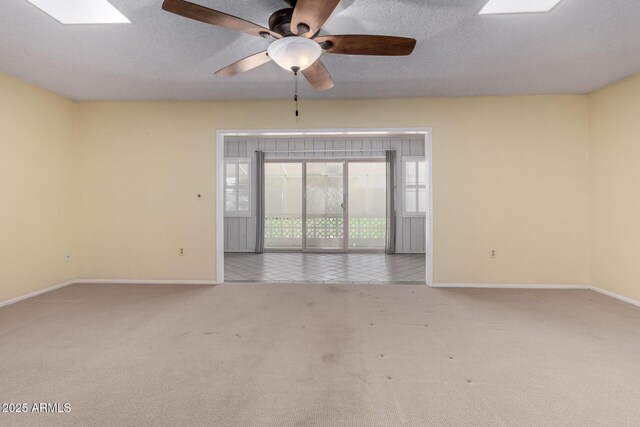 unfurnished room featuring baseboards, ceiling fan, carpet, a skylight, and a textured ceiling