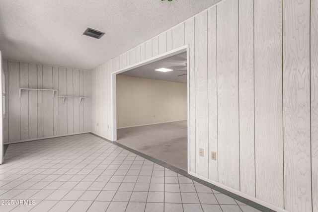 carpeted empty room featuring visible vents, a textured ceiling, wooden walls, and tile patterned flooring