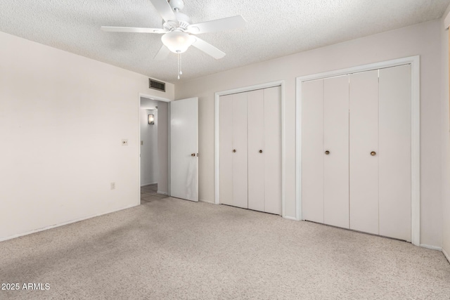 unfurnished bedroom featuring visible vents, two closets, ceiling fan, carpet flooring, and a textured ceiling