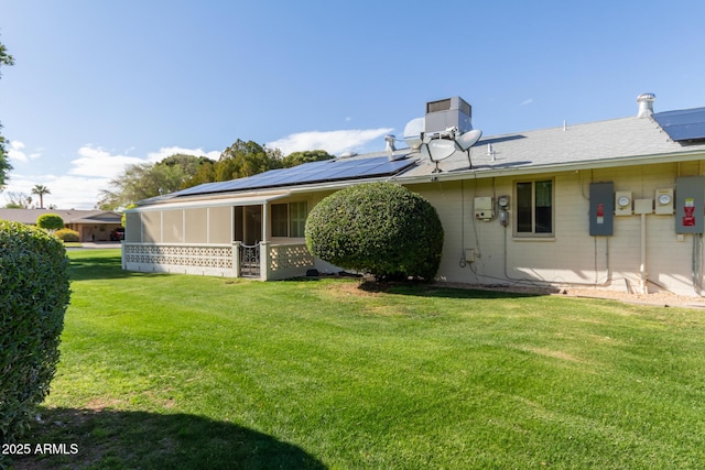 back of property with a yard, roof mounted solar panels, and a sunroom