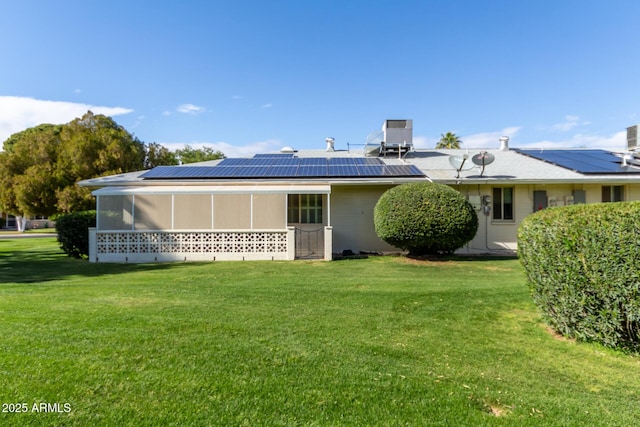 rear view of property featuring roof mounted solar panels, a lawn, and a sunroom