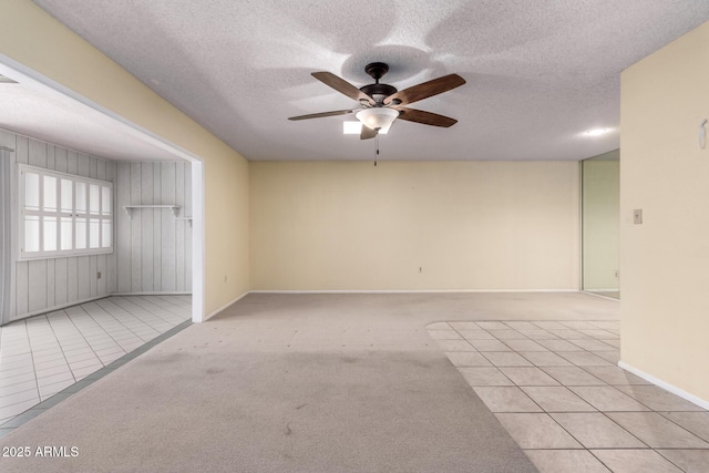 spare room featuring a textured ceiling, light tile patterned floors, baseboards, ceiling fan, and light carpet