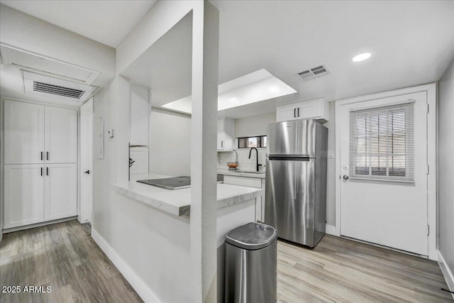 kitchen with kitchen peninsula, sink, white cabinetry, black electric cooktop, and stainless steel refrigerator