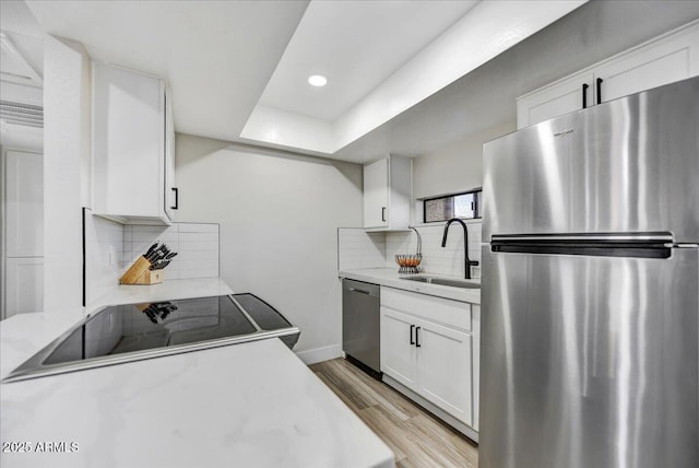 kitchen with appliances with stainless steel finishes, sink, white cabinets, light hardwood / wood-style flooring, and backsplash