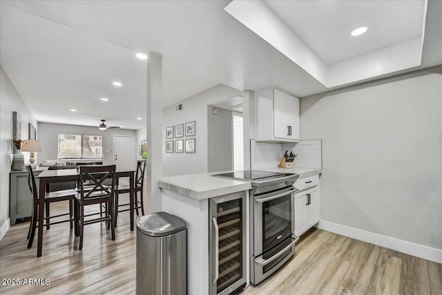 kitchen with beverage cooler, white cabinets, tasteful backsplash, light wood-type flooring, and stainless steel electric range