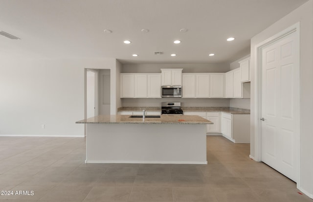 kitchen with an island with sink, white cabinetry, appliances with stainless steel finishes, and light stone counters