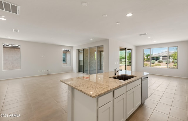 kitchen featuring light stone counters, a kitchen island with sink, sink, white cabinets, and stainless steel dishwasher