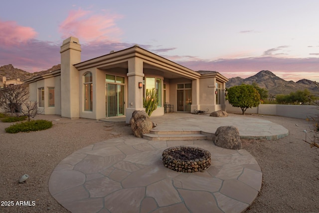 back house at dusk featuring a mountain view, an outdoor fire pit, and a patio area