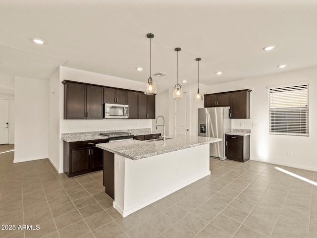 kitchen with light stone countertops, stainless steel appliances, an island with sink, sink, and dark brown cabinets