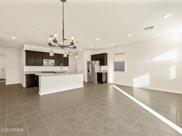 kitchen featuring appliances with stainless steel finishes, a kitchen island with sink, dark brown cabinets, tile patterned floors, and hanging light fixtures