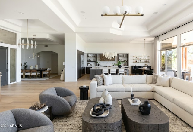 10795 E Sutherland Way, Scottsdale, AZ 85262 - living room with arched walkways, an inviting chandelier, a raised ceiling, and light wood-style floors