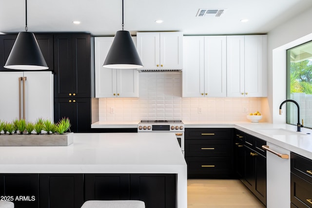 kitchen with high quality appliances, tasteful backsplash, sink, white cabinets, and hanging light fixtures