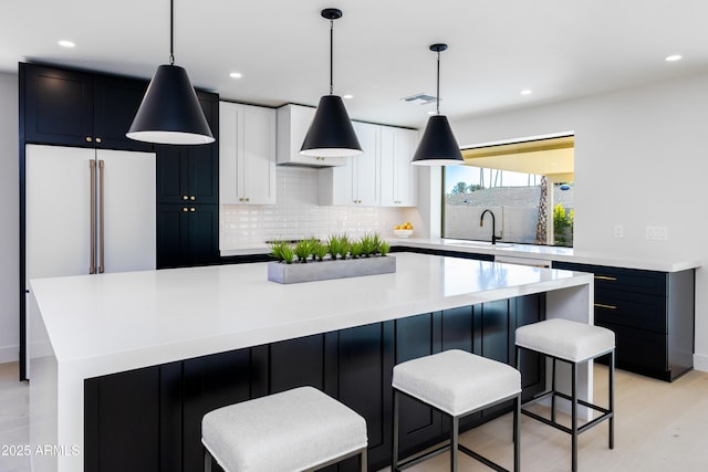 kitchen with tasteful backsplash, white cabinets, hanging light fixtures, a large island, and light wood-type flooring