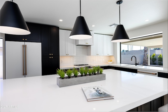 kitchen with sink, high end fridge, white cabinetry, decorative backsplash, and decorative light fixtures