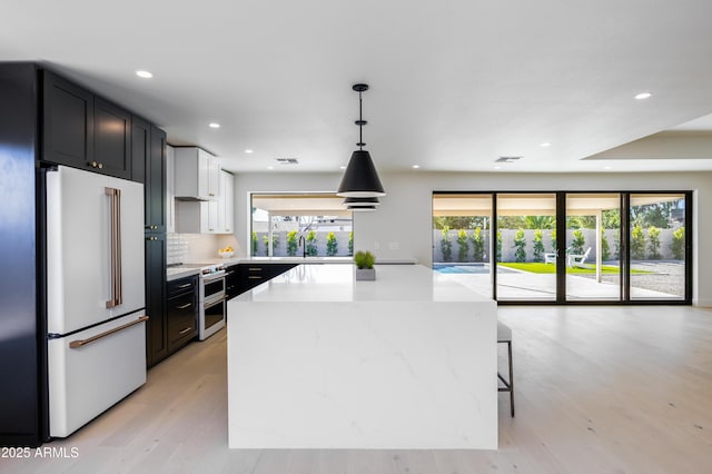 kitchen featuring decorative light fixtures, high end white refrigerator, double oven range, a center island, and light hardwood / wood-style flooring