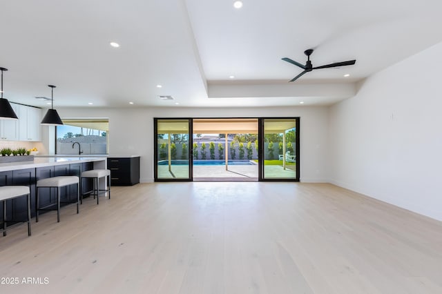 unfurnished living room featuring a tray ceiling, sink, ceiling fan, and light hardwood / wood-style flooring