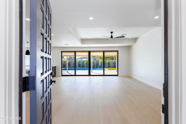 unfurnished living room with ceiling fan, a tray ceiling, and light hardwood / wood-style flooring