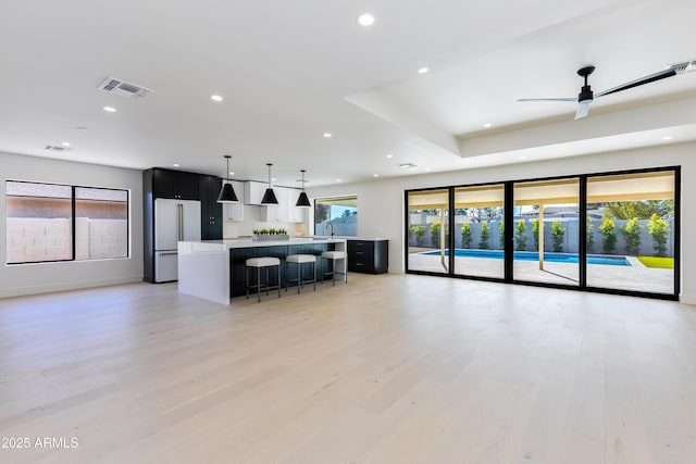 kitchen with a kitchen bar, hanging light fixtures, high end fridge, light wood-type flooring, and a spacious island