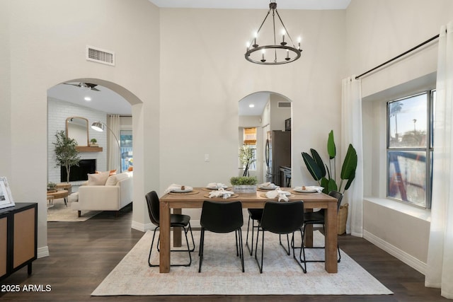 dining room featuring a high ceiling, a fireplace, dark hardwood / wood-style floors, and ceiling fan with notable chandelier