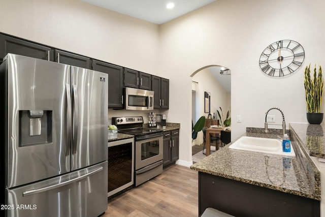 kitchen with stone counters, sink, stainless steel appliances, and light hardwood / wood-style floors