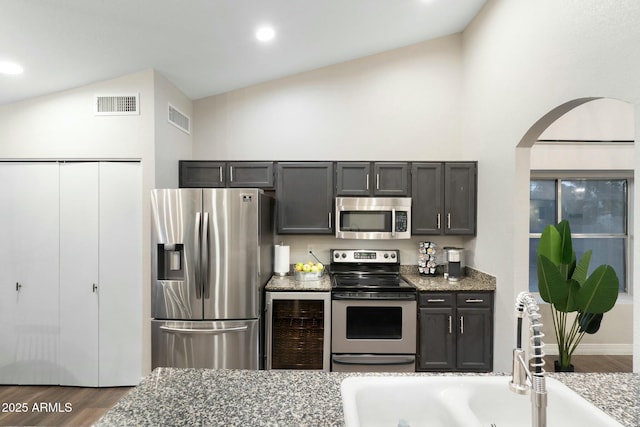 kitchen with wine cooler, dark stone countertops, lofted ceiling, and appliances with stainless steel finishes