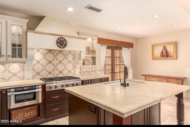 kitchen featuring a kitchen island with sink, appliances with stainless steel finishes, sink, dark brown cabinets, and custom exhaust hood