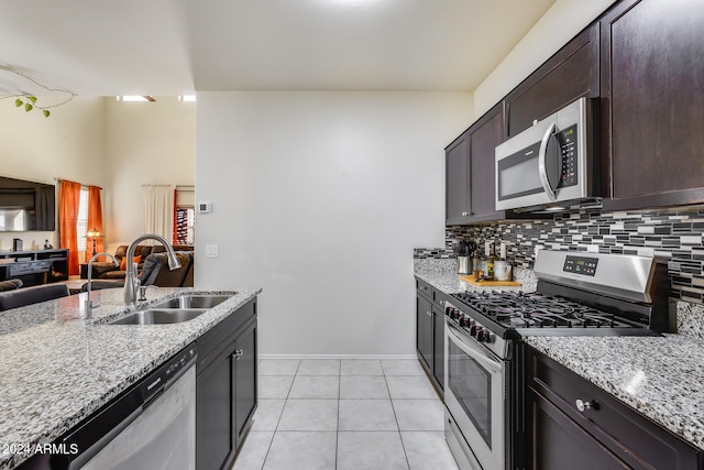 kitchen featuring appliances with stainless steel finishes, light tile patterned flooring, dark brown cabinets, light stone countertops, and sink