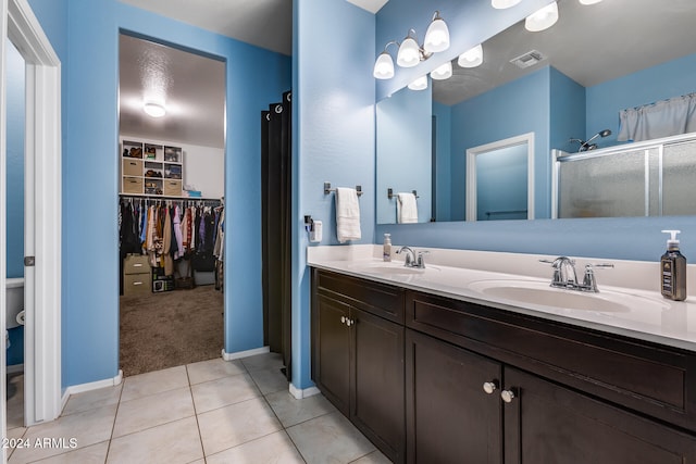 bathroom with a shower with shower door, vanity, and tile patterned flooring