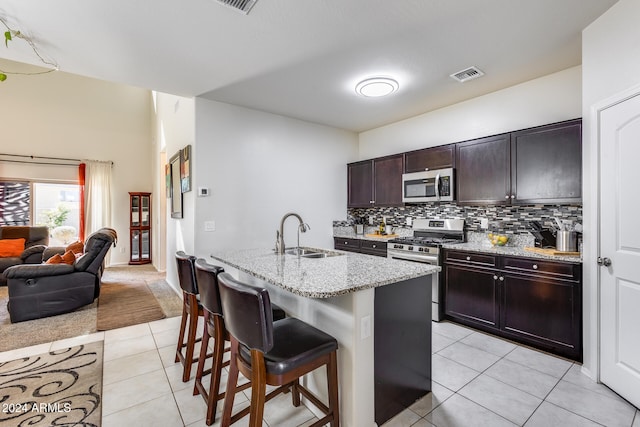 kitchen featuring a kitchen bar, sink, light tile patterned flooring, appliances with stainless steel finishes, and an island with sink