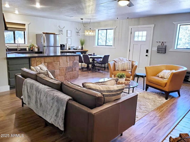 living room featuring light hardwood / wood-style flooring, ceiling fan with notable chandelier, plenty of natural light, and a textured ceiling