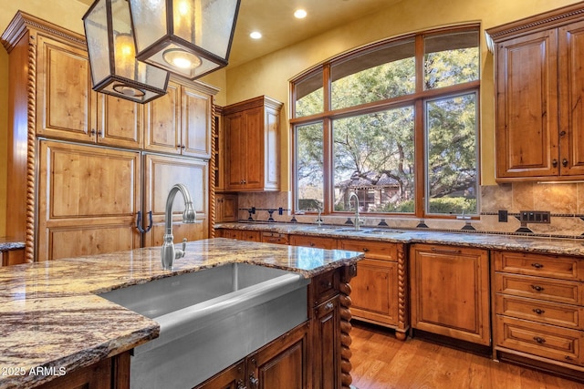 9980 E Charter Oak Rd, Scottsdale, AZ 85260 - kitchen featuring sink, light stone counters, tasteful backsplash, decorative light fixtures, and light hardwood / wood-style flooring