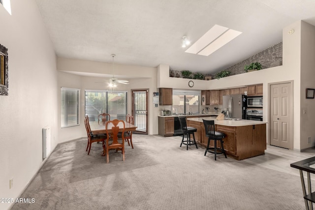 dining room featuring light carpet, high vaulted ceiling, a ceiling fan, and a skylight