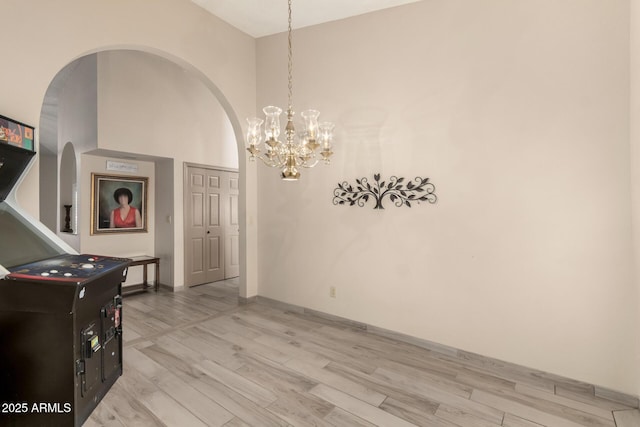interior space with baseboards, an inviting chandelier, a high ceiling, arched walkways, and light wood finished floors