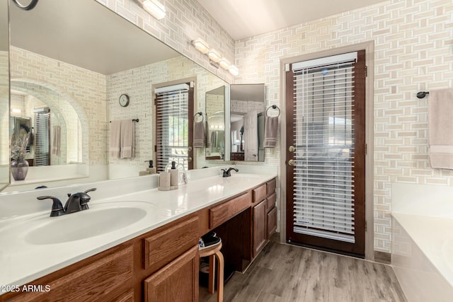 full bath with a bathing tub, wood finished floors, double vanity, and a sink