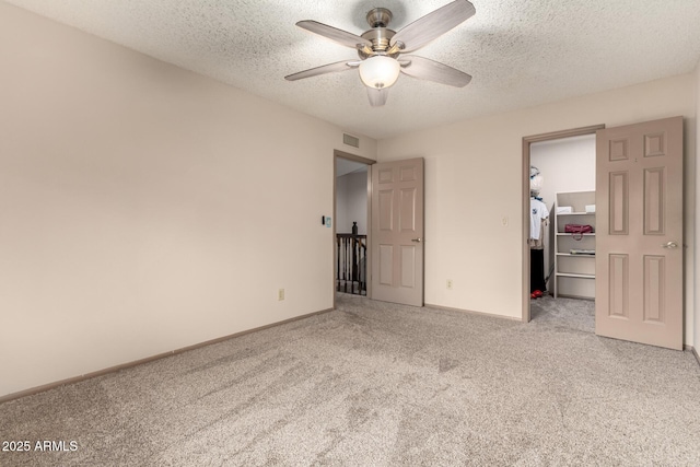 unfurnished bedroom with a closet, a spacious closet, a textured ceiling, carpet floors, and visible vents
