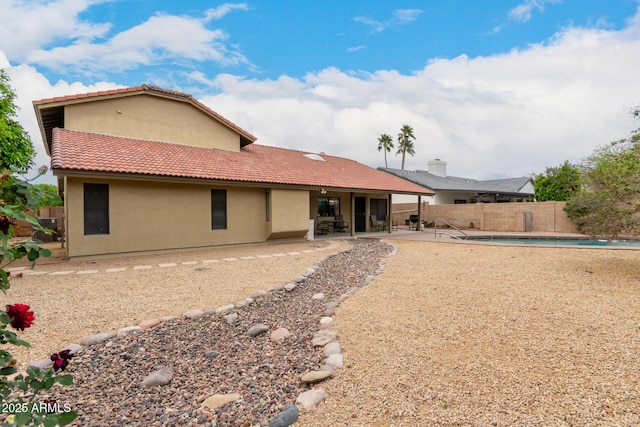 rear view of property featuring a fenced backyard, a tile roof, a patio, stucco siding, and a fenced in pool